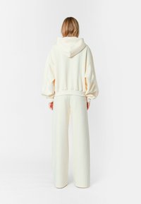 Sudadera color crema con capucha y ajuste holgado, combinada con pantalones anchos a juego. Tejido suave con una textura lisa.