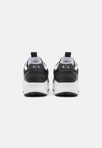 Black and white sneakers with a textured mesh upper and smooth leather accents, featuring a pull tab and logo on the heel.