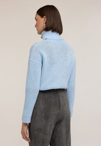 Ljusblå stickad tröja med hög hals och öppen mesh-mönster, kombinerad med mörkgrå kordflossa-byxor. Looken har texturerade detaljer.