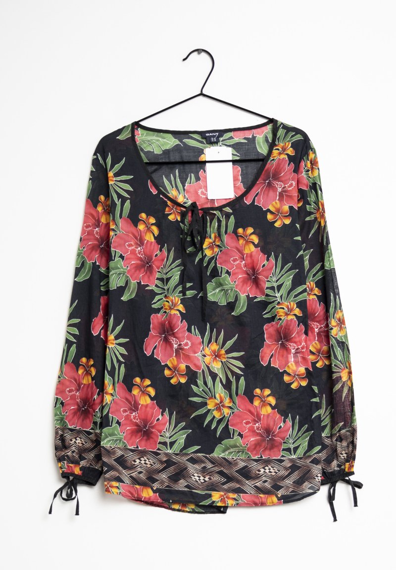 Blusa floreale con maniche lunghe, sfondo nero, grandi fiori rossi e gialli, polsini arricciati con motivo e dettaglio a fiocco sul colletto.