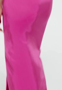Abito rosa aderente con una texture liscia e lucida e una leggera brillantezza. Il tessuto si adagia vicino al corpo, mettendo in risalto la silhouette.