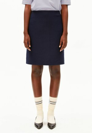 Personne portant une jupe bleu marine au genou, des chaussettes blanches rayées, des chaussures noires pointues et une chemise bleu clair à manches courtes.
