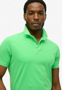 Polo shirt in cotone verde con colletto, dotato di una patta a due bottoni e maniche corte, texture liscia e design aderente.