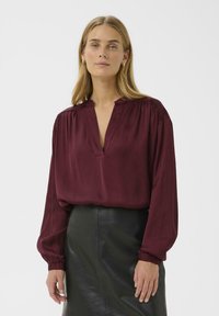 Burgundy silk blouse with a deep V-neck, gathered shoulders, and long sleeves with elastic cuffs, paired with a black leather skirt.