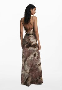 Barna és krémszínű, tarka maxi ruha vékony pántokkal, mély hátrésszel és egy drámai sziluettel, amelyet átlós mintázat vonalak díszítenek.