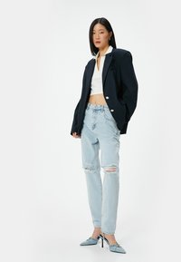 Marinblazer med silverknappar, vit kortärmad skjorta, ljusblå slitna jeans och blå klackskor. Platta texturer och avslappnad passform.