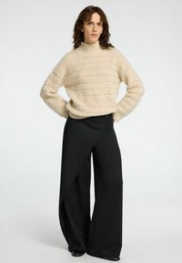 Beige, stickad tröja med hög krage och horisontella ränder; matchad med vida, svarta byxor med asymmetrisk omslag.