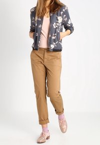 Giacca bomber grigia con motivo floreale, top rosa chiaro, pantaloni corti marroni, calze rosa e scarpe beige lucide. Un outfit casual con diverse trame.