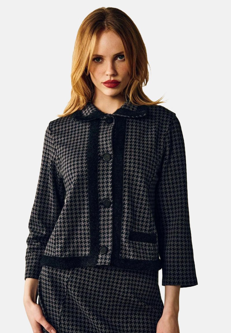 Sort og grå houndstooth-jakke med krave, tre knapper og en brystlomme. Struktureret stof med en tætsiddende pasform.
