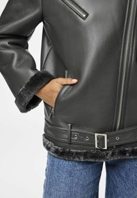 Giacca in pelle grigia scura con collo e polsini in pelliccia finta, dotata di tasche con zip e vita regolabile con cintura. Finitura testurizzata e design elegante.