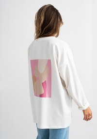 Felpa bianca a maniche lunghe con un design astratto colorato in tonalità di rosa e beige sul retro, che presenta una vestibilità rilassata e una texture morbida.