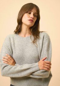 Pull léger gris en tissu doux et texturé, avec un col rond et des poignets côtelés, qui présente une coupe décontractée.