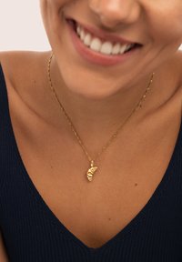 Collar de cadena trenzada en oro con un colgante de concha en espiral de superficie texturizada, usado sobre una blusa de rayas azul oscuro.