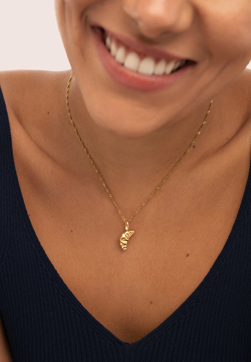 Collar de cadena trenzada en oro con un colgante de concha en espiral de superficie texturizada, usado sobre una blusa de rayas azul oscuro.