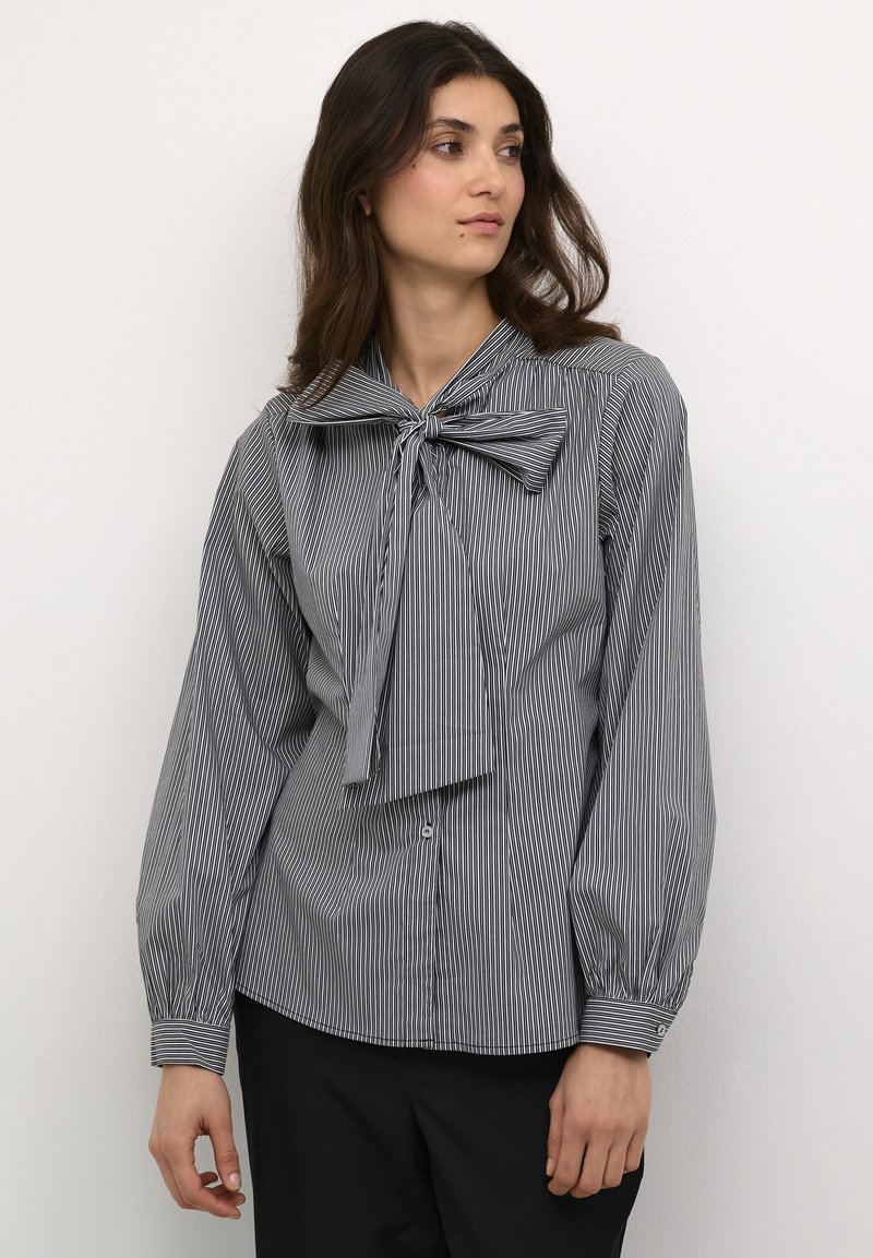 Camicia a righe bianca e nera con cravatta a farfalla al colletto, maniche lunghe e design aderente. Tessuto testurizzato.