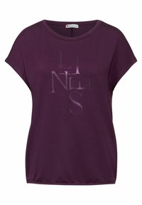 Camiseta corta de manga en color púrpura, hecha de una tela suave, que presenta un sutil estampado gráfico de la palabra "LINES" en diferentes tonalidades. Cuello redondo clásico.