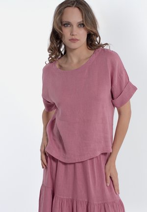 Haut à manches courtes, ample, en lin rose doux, avec un col rond et des manches repliées, associé à une jupe à volants assortie.