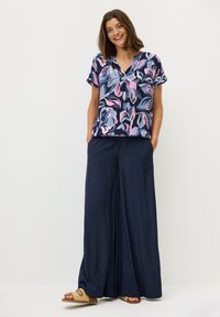 Blusa a maniche corte con stampa floreale nei colori navy, rosa e azzurro; abbinata a pantaloni navy dalla vestibilità ampia e sandali neutri.