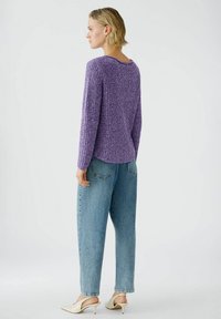 Lila strukturiertes Strickpullover, lockere Passform, runder Ausschnitt, kombiniert mit hellblauen Denim-Jeans und cremefarbenen Mules, von hinten betrachtet.