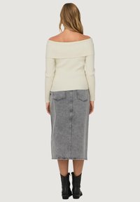 Ribbed off-the-shoulder cream sweater with long sleeves paired with a gray denim midi skirt featuring a back slit and visible stitching. Black ankle boots.