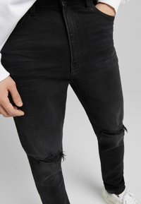 Svarta denimjeans med slim fit, med slitna knän och en texturerad yta. Stylar med standard midja och sidofickor.