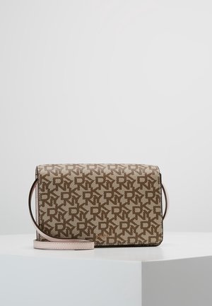 Sac bandoulière rectangulaire avec un motif répétitif de logo "DKNY" beige et marron, doté d'une sangle réglable rose clair, posé sur une surface blanche.