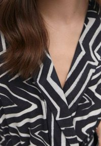 Tela de patrón en blanco y negro con un diseño de zigzag, que presenta un escote en V profundo y una textura suave. Enfoque en los detalles del collar y el escote.
