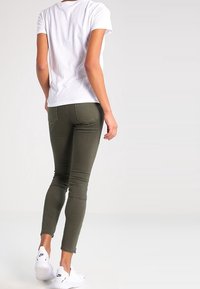 Gröna skinny jeans i denim, med medelhög midja och tajt passform, ihopparade med en enkel vit t-shirt och vita sneakers.