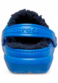 Blaue Crocs mit einem weichen schwarzen Fleece-Futter, einem Riemen hinten, strukturiertem Profil und glatter Oberfläche. Merkmale sind die abgerundete Form und das Logo-Detail.