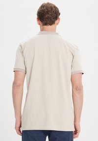 Béžová polo košile s krátkým rukávem, vybavená texturovaným límcem a manžetami. Tkanina vypadá hladce a má uvolněný střih.