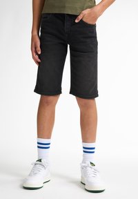 Pantalones cortos de denim negro con corte recto, dobladillo vuelto y un ligero desgaste. Llevados con zapatillas blancas y calcetines a rayas.