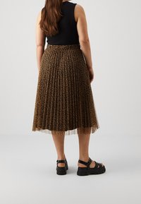 Svart ärmlös topp i kombination med en knälång, veckad tyllkjol med ett brunt leopardprinsdesign och svarta klumpiga sandaler.