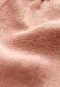Textielstof in een zachte perzikkleur, met een gladde, licht gestructureerde oppervlakte en een subtiel weefpatroon.