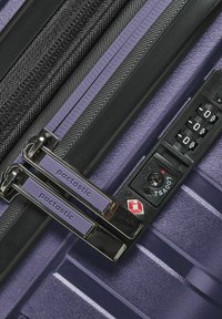 Maleta rígida morada con cremallera negra, doble tirador de cremallera de metal etiquetados "pactastic" y un candado de combinación de la TSA en negro.
