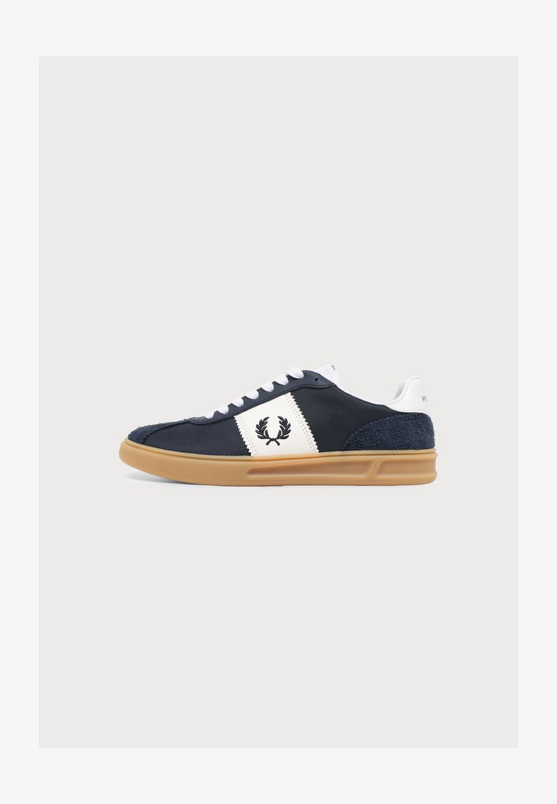 Baskets bleu marine avec lacets blancs, panneau latéral blanc avec logo couronne de laurier noir, et semelle marron clair sur fond uni.