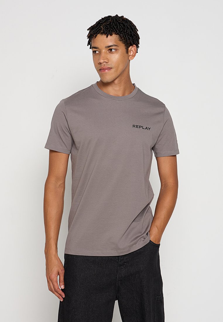 Graues Baumwoll-T-Shirt mit Rundhalsausschnitt, featuring ein kleines schwarzes "REPLAY"-Logo auf der linken Brust. Kurze Ärmel; glatte Textur.