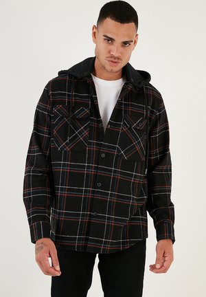 Zwarte en rode geruite flanellen shirt met een zwarte capuchon, voorzien van twee borstzakken en knoopsluiting, gemaakt van zachte, textuurrijke stof.