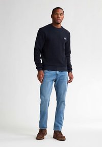 Granatowa teksturowana bluza z prążkowanymi mankietami i paskiem u dołu, zestawiona z jasnoniebieskimi jeansami i brązowymi botkami za kostkę. Codzienny strój o luźnym kroju.