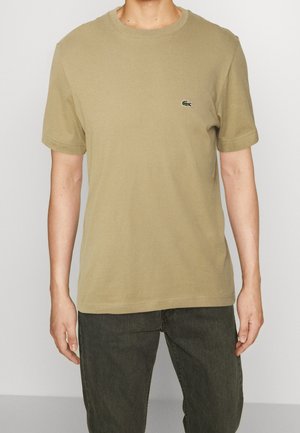 Beige Baumwoll-T-Shirt mit Rundhalsausschnitt und kurzen Ärmeln, mit einem grünen Lacoste Krokodil-Logo auf der linken Brust.