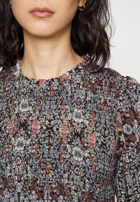 Musta kukkakuosiset mekko, jossa on punaisia ja sinisiä yksityiskohtia. Mekossa on pleatattu pinta ja pyöreä pääntie, jossa on lyhyet puffihihat.