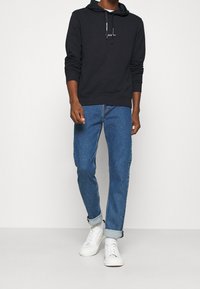 Felpa nera in cotone con lacci, abbinata a jeans in denim blu e sneakers bianche, con orli arrotolati. Design semplice nel complesso.