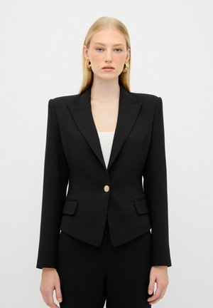 Blazer negro ajustado con solapas muescas, cierre de botón dorado y dos bolsillos frontales. Textura suave, forma ajustada y diseño minimalista.