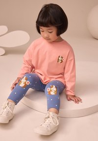 Cămașă roz deschis cu mâneci lungi și broderie mică cu un animal, asortată cu colanți albaștri cu un model de porcușor de Guineea și buline albe.