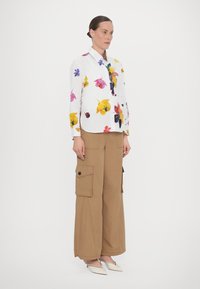 Floral-patterned white shirt with long sleeves, paired with beige cargo pants featuring side pockets and a loose fit.