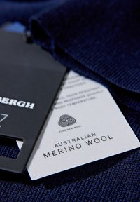 Marineblaues Merinowollkleidungsstück mit Etiketten, die "Reine neue Wolle" und "Australische Merinowolle" anzeigen. Die Textur wirkt weich und fein.