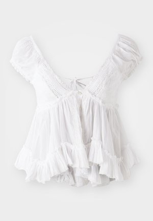 Biela blúzka s krátkymi nafúknutými rukávmi, čipkovými detailmi, viazaním na krku a volánovým lemom. Vyrobená z ľahkej, textúrovanej látky.