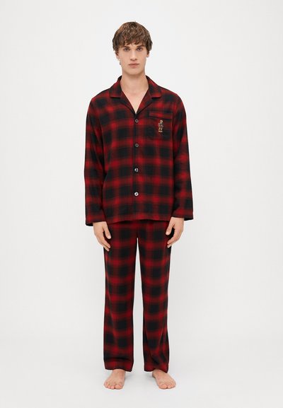 Conjunto de pijama de franela a cuadros rojos y negros, que incluye una camisa de manga larga y pantalones, con un bolsillo en el pecho que detalla un logo. Textura suave, ajuste holgado.