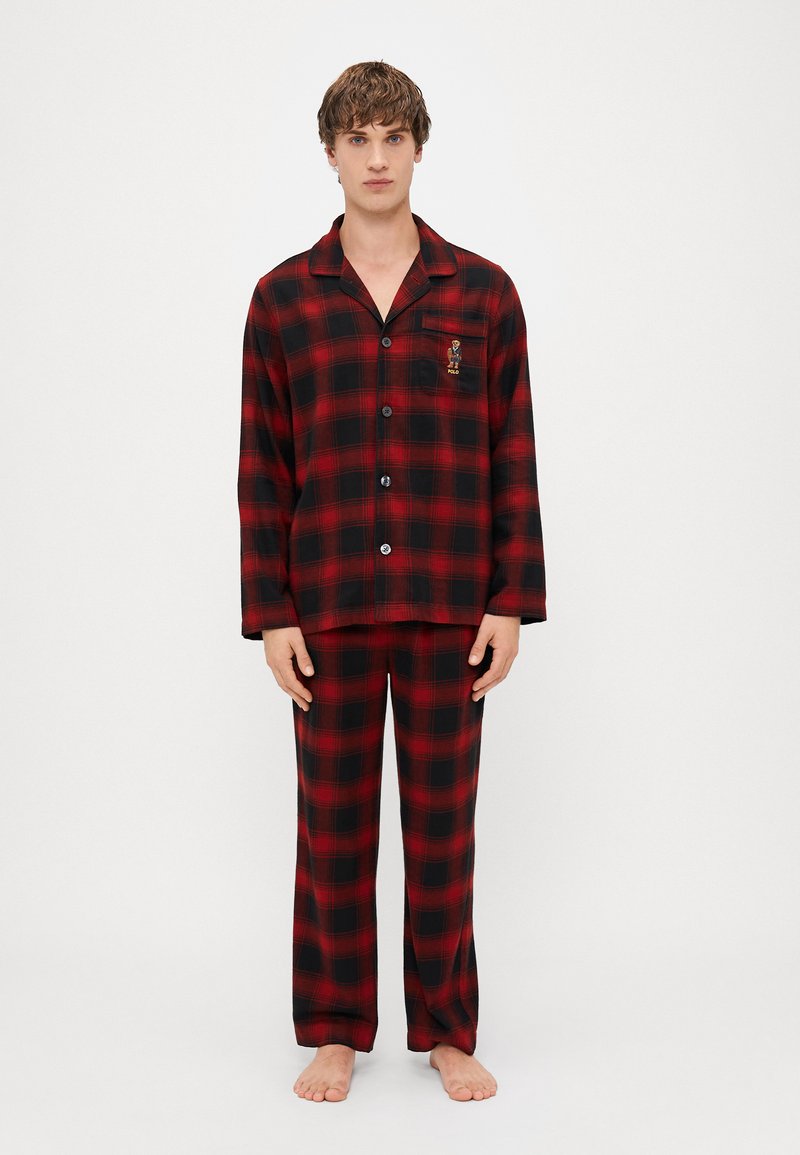 Pajama set od crveno-crne karirane flanele s dugim rukavima i hlačama, s džepom na prsima koji ima detalj loga. Glatka tekstura, široki kroj.