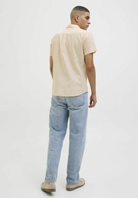 Korte mouwen, perzikkleurig shirt met een button-down kraag, gecombineerd met lichtblauwe jeans en beige schoenen, met een ontspannen pasvorm.