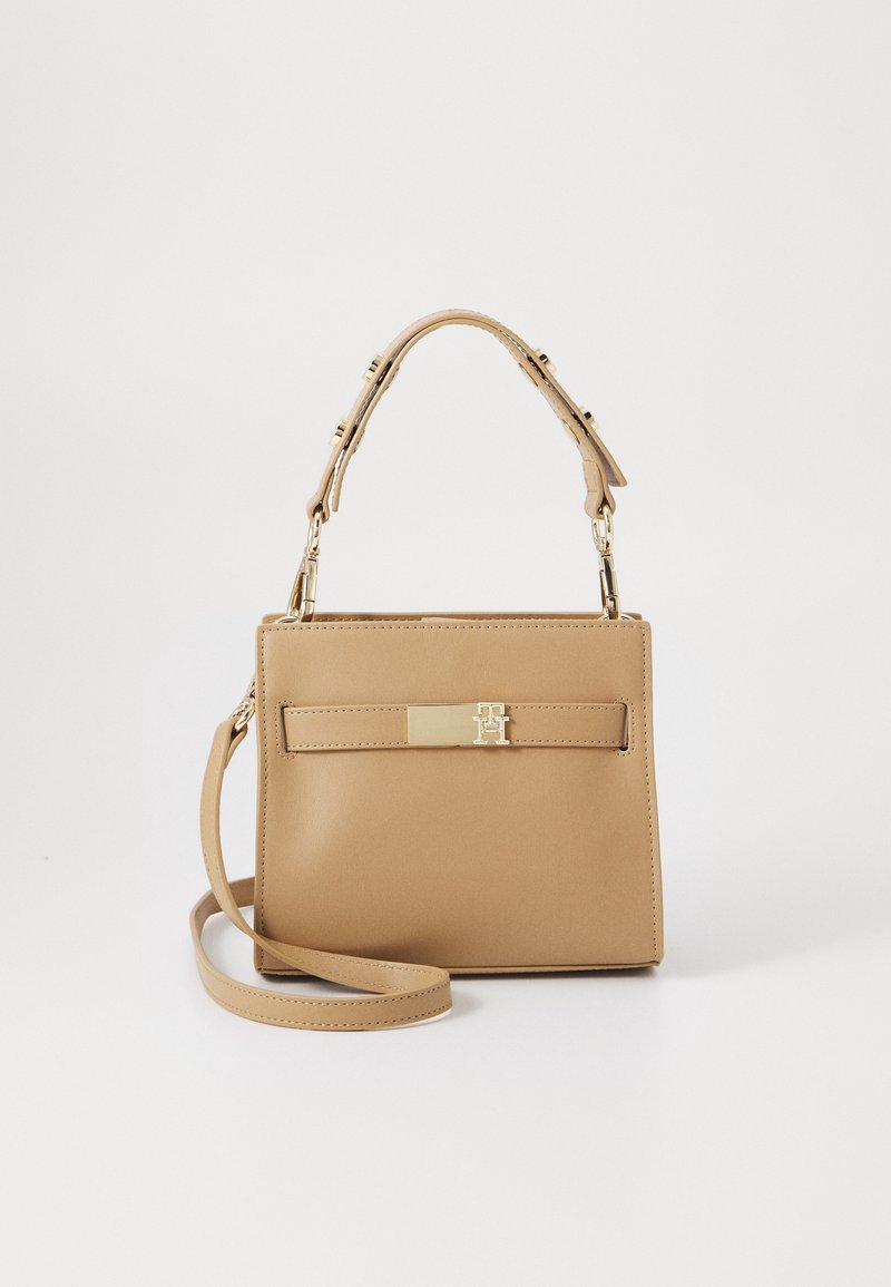 Sac à main structuré beige avec poignée supérieure et bandoulière amovible, doté d'un fermoir rectangulaire doré et d'un minimalisme dans les détails.